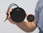 Person holding a black portable speaker with close-up of textured surface