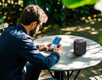 Man using a smartphone with a wireless speaker on a table outdoors