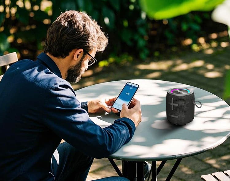 Man using a smartphone with a wireless speaker on a table outdoors