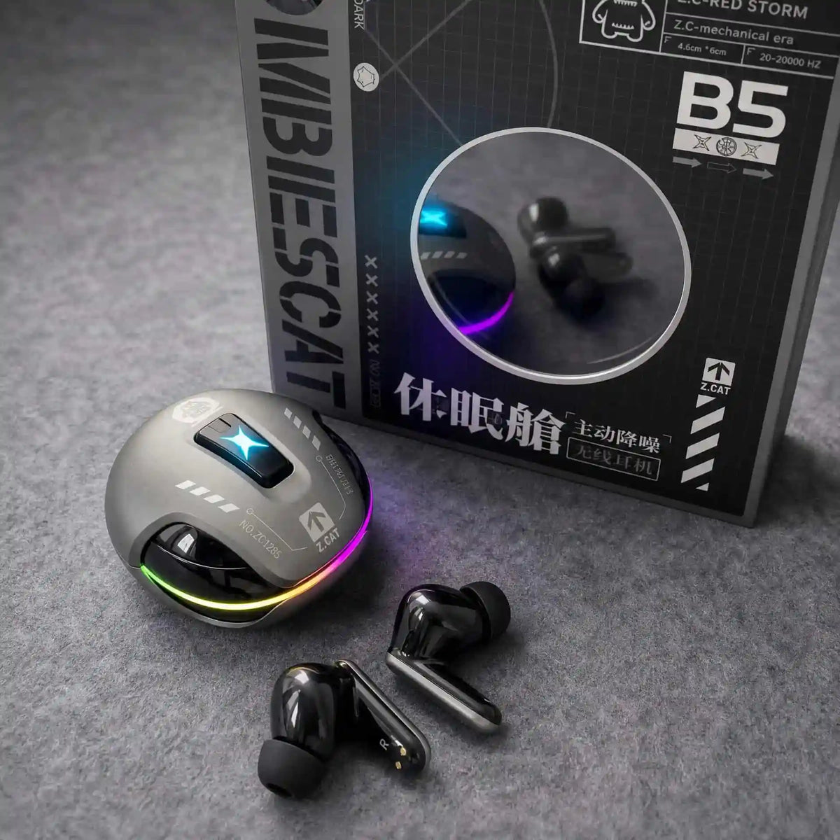 A pair of black wireless earbuds and a matching charging case with RGB lighting are shown in front of their product box on a gray textured surface. The box is branded MIBIESCAT and features Chinese text.